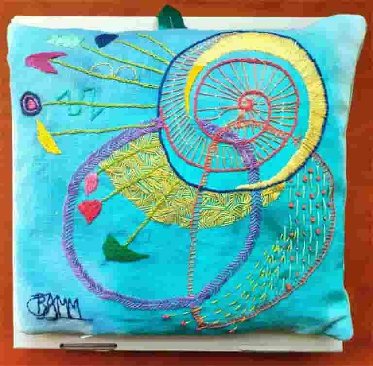 Hand embroidery on painted turquoise linen expressing the joy of life