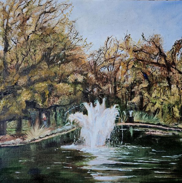 A Victorian pond with a central fountain set in parkland. The water forms spray and white ripples in the water. Autumn trees in the background. 