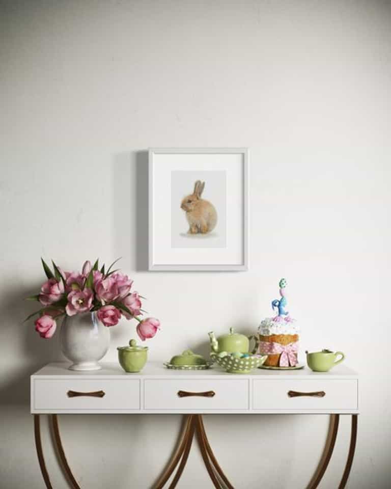 Coloured pencil drawing by Katrina Thompson of little easter bunny above a table set with flowers and easter decorations 