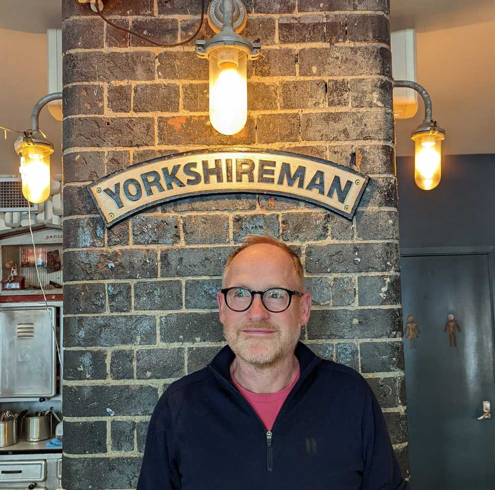The artist Matthew in a Café in London posing under a sign that says Yorkshireman